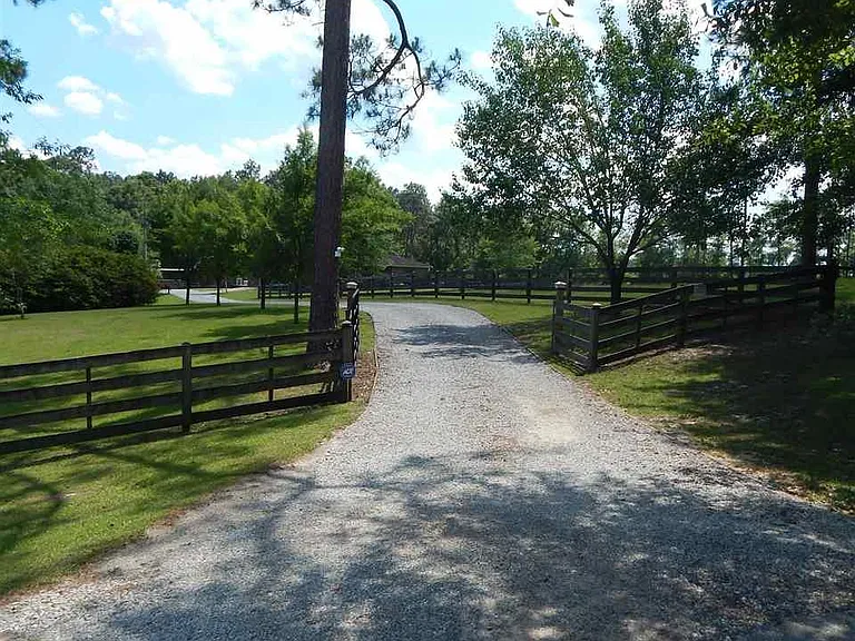 A wide green fenced training pasture at golden hour, with a long fence line running toward pines and low haze.